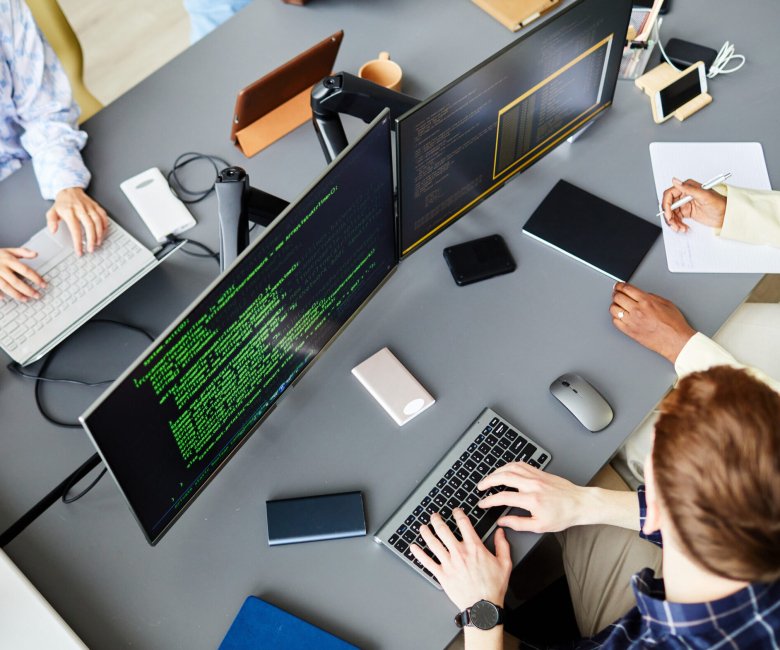 High angle view of group of programmers sitting at table in front of computer monitors and working with codes